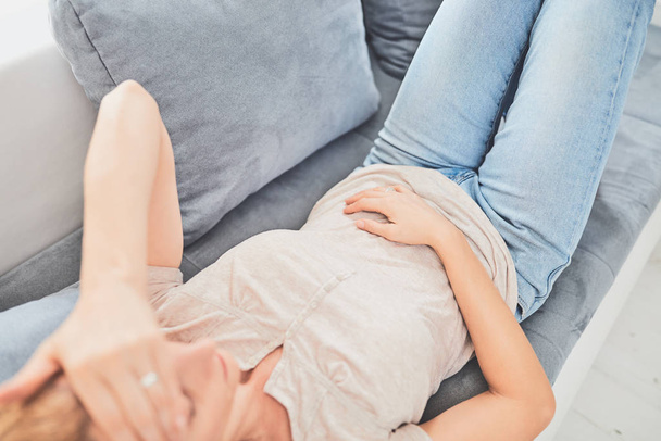 Mujer con problemas de estómago / problemas mientras está acostada en el sofá
. - Foto, imagen
