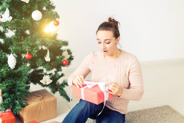 La Navidad, la Navidad, el invierno, el concepto de la felicidad - la muchacha abre el regalo en el fondo del árbol de Navidad. Feliz joven celebrando la Navidad
 - Foto, Imagen