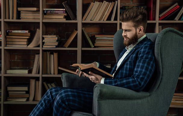 Κομψός άνδρας με κοστούμι κάθεται σε vintage δωμάτιο και το βιβλίο ανάγνωσης. Άνθρωπος της μόδας. - Φωτογραφία, εικόνα