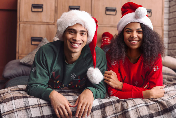Happy African-American couple in Santa hats at home on Christmas eve - Photo, Image