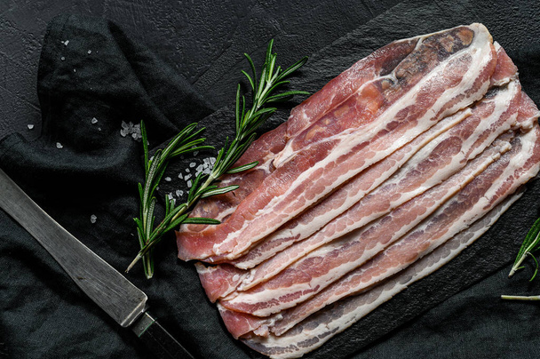 Bacon on a stone cutting Board. Pork meat. Black background. Top view - Foto, imagen