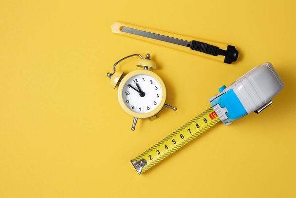 Measuring tape, cutter knife and clock isolated over yellow bakground. Carpenter and Construct concept. - Photo, Image