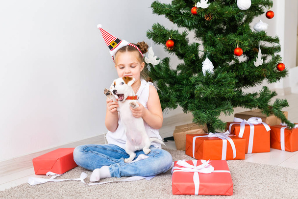 Weihnachts-, Haustier- und Urlaubskonzept - Kind mit Weihnachtsmütze und Jack Russell Terrier Welpe - Foto, Bild