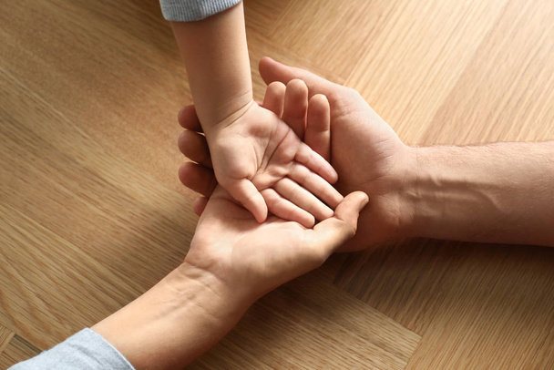 Happy family holding hands on wooden background, closeup - 写真・画像