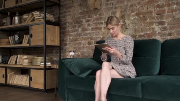 Woman scrolling on tablet at home, uses technology. Woman sits on sofa, she's using tablet computer. Woman touching Digital Tablet at home.  - Materiał filmowy, wideo