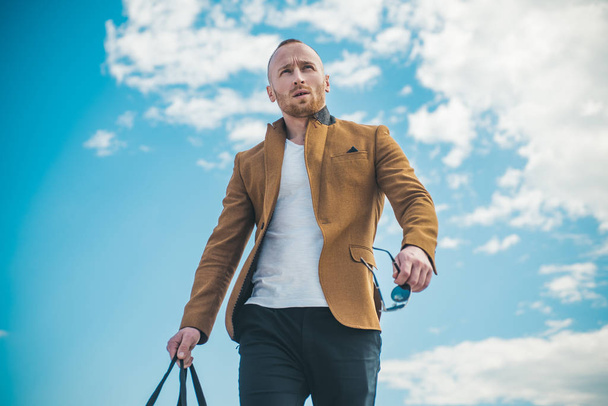 Man with confident face and brutal style. Advertising for clothing store. Standing on the pure blue sky background next to copyspace. Fashionable man in leather jacket. - Foto, immagini