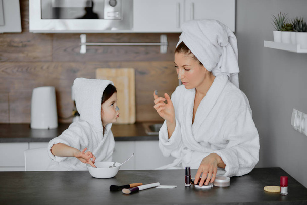 admirable woman and child in towels and bathrobes use beauty masks - 写真・画像