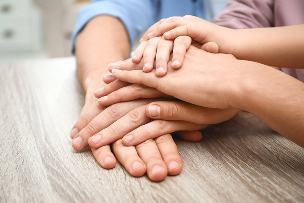 Happy family holding hands at wooden table indoors, closeup view - Photo, Image