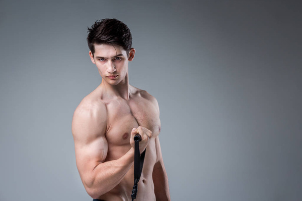 Muscular fitness young male antique perfect muscles six packs of abs and bare chest. Bodybuilder model trains with a stretching elastic against a dark background in the studio. Workout training gym - Photo, Image
