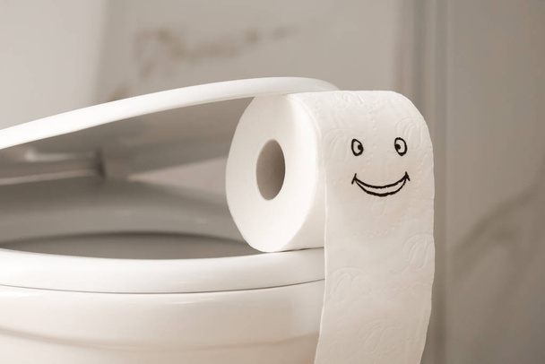 Roll of paper with funny face on toilet bowl in bathroom, closeup - Fotoğraf, Görsel