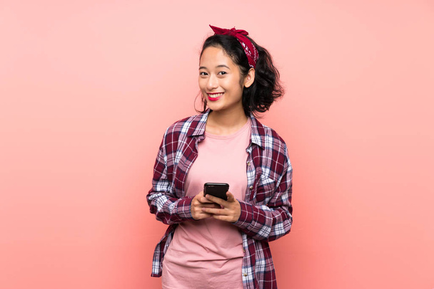 Азійська молода жінка через ізольований рожевий фон відправляє повідомлення з мобільним телефоном - Фото, зображення