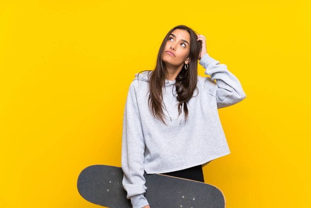 Young skater woman over isolated yellow background having doubts and with confuse face expression - Foto, Imagen