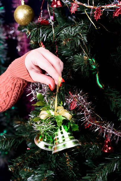 Girl decorates a Christmas tree with green bells. - Foto, imagen