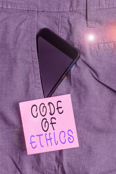 Handwriting text Code Of Ethics. Concept meaning Moral Rules Ethical Integrity Honesty Good procedure Smartphone device inside formal work trousers front pocket near note paper. - Photo, Image
