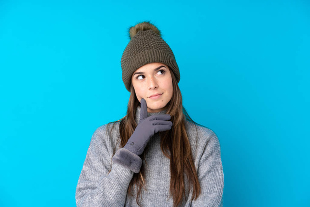 Chica adolescente con sombrero de invierno sobre fondo azul aislado pensando en una idea - Foto, imagen