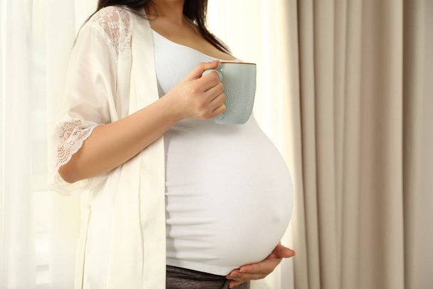 Pregnant woman with cup of hot drink at home, closeup - Foto, Bild