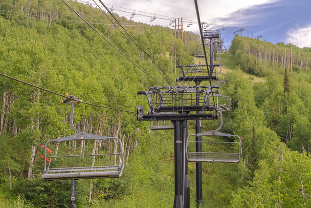 Председатели на тросах над лыжной горой с густыми зелеными деревьями в межсезонье
 - Фото, изображение