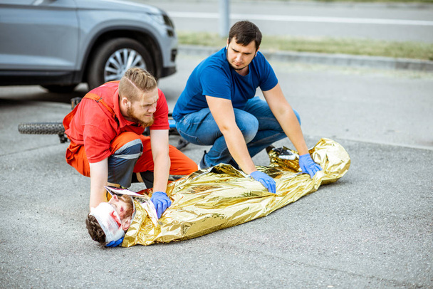 Medycy pokrywają ofiarę kocem termicznym po wypadku. - Zdjęcie, obraz