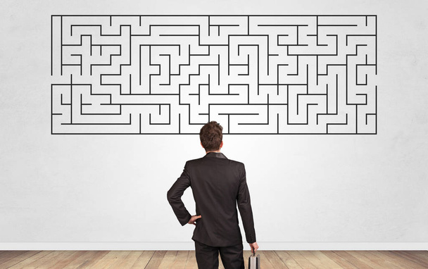 Businessman looking to a maze on a wall - 写真・画像