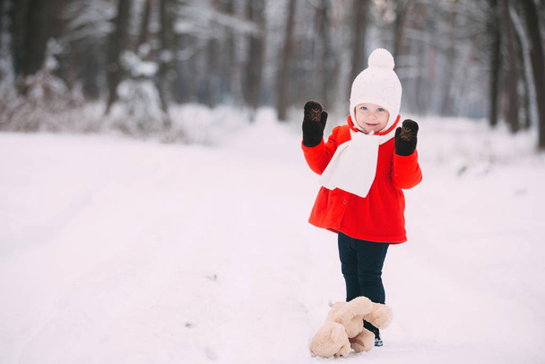 Mała dziewczynka w czerwonym płaszczu z misiaczkiem bawiącym się w zimowy dzień. dziewczyna gra w śniegu - Zdjęcie, obraz