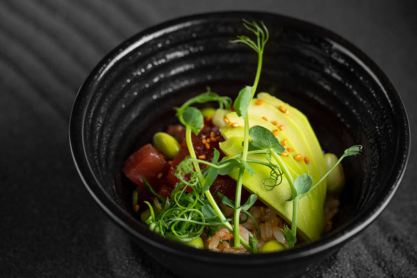 Poke bowl Raw fish salad Asian trendy food with soy beans edamame, rice, avocado and lettuce in bowl on dark background - Zdjęcie, obraz