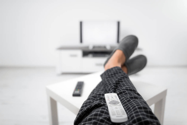 Homem bebendo suco de refrigerante e olhando para a TV com pernas na mesa
 - Foto, Imagem