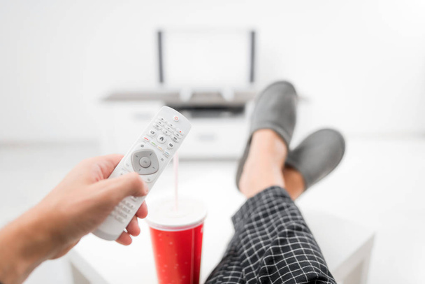 Чоловік п'є содовий сік і дивиться телевізор з ногами на столі
 - Фото, зображення