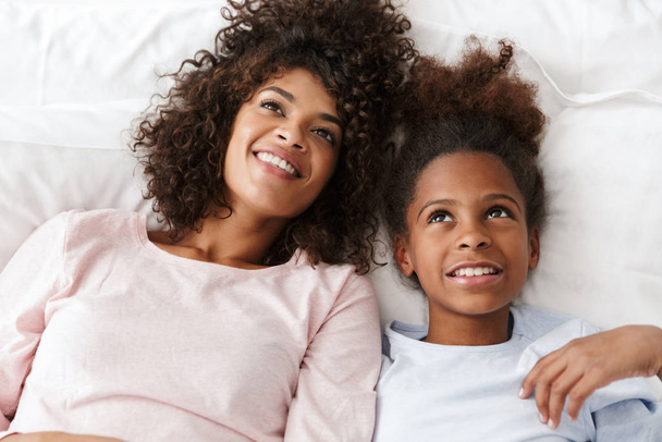 Image of cheerful african american woman and her daughter lying  - Foto, Imagem