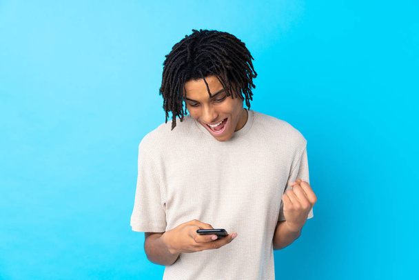 Genç Afrikalı Amerikalı bir adam mavi arka planda şaşırdı ve bir mesaj gönderiyor. - Fotoğraf, Görsel