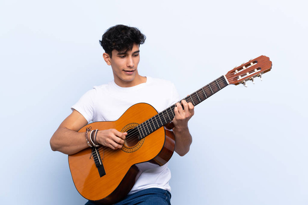 Joven argentino con guitarra sobre fondo azul aislado - Foto, imagen