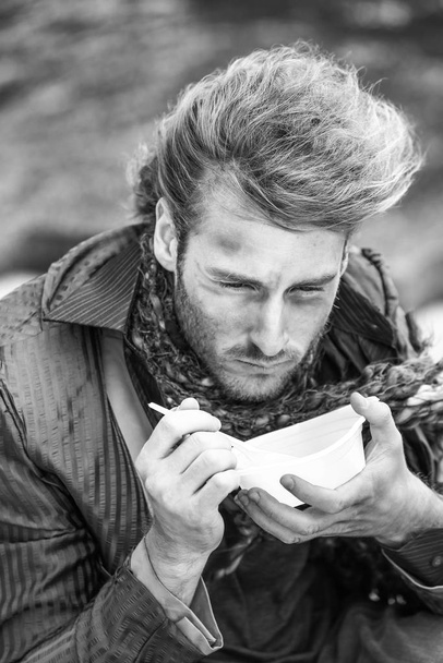 Retrato en blanco y negro de un pobre indigente comiendo comida al aire libre
 - Foto, Imagen