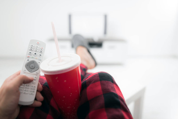 Hombre bebiendo jugo de soda y mirando televisión con piernas en la mesa
 - Foto, imagen