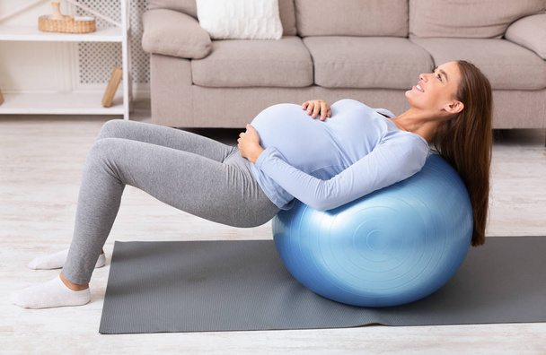 Pregnant girl working out with fitness ball at home - Fotó, kép