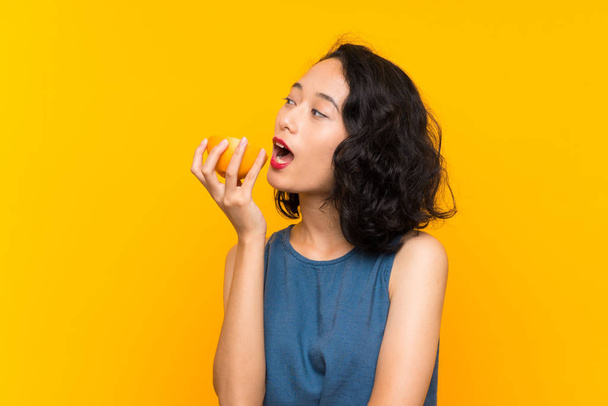 junge asiatische Mädchen mit einer Grapefruit über isolierten orangefarbenen Hintergrund - Foto, Bild