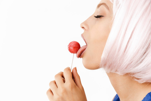 Photo in profile of relaxed happy woman wearing pink wig licking lollipop - Fotó, kép