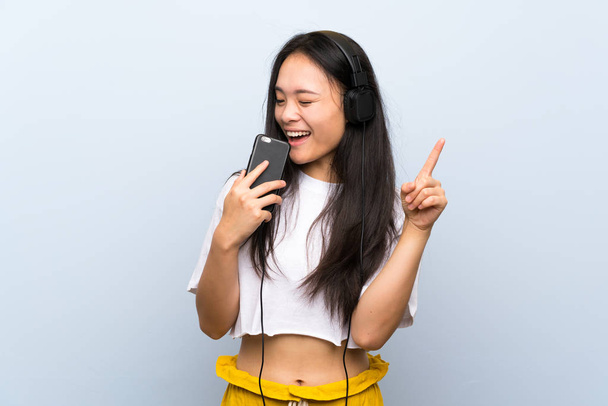 Teenager asian girl listening music over isolated blue wall singing - Foto, Imagem