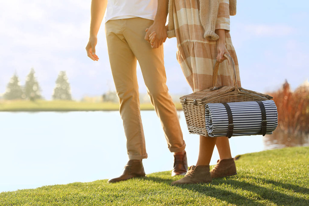 Pareja joven con cesta de picnic cerca del lago en el día soleado, primer plano
 - Foto, imagen