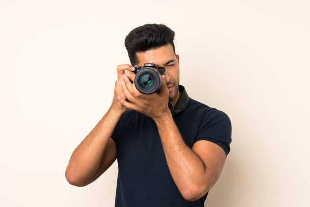 Jonge knappe man over geïsoleerde achtergrond met een professionele camera - Foto, afbeelding