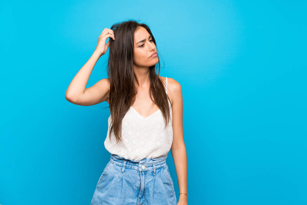 Young woman over isolated blue background having doubts while scratching head - Photo, image