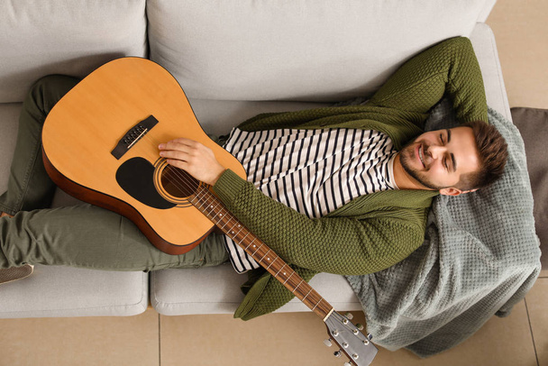 Красивий молодий чоловік з гітарою розслабляється вдома
 - Фото, зображення