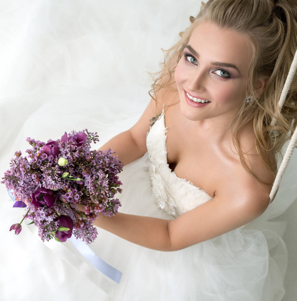 Young bride in studio on swing with fine bouquet - Foto, imagen