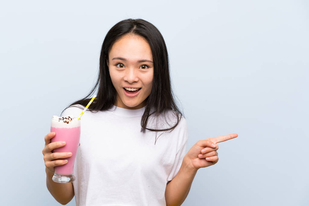 Teenager asian girl holding a strawberry milkshake surprised and pointing finger to the side - Foto, Imagem