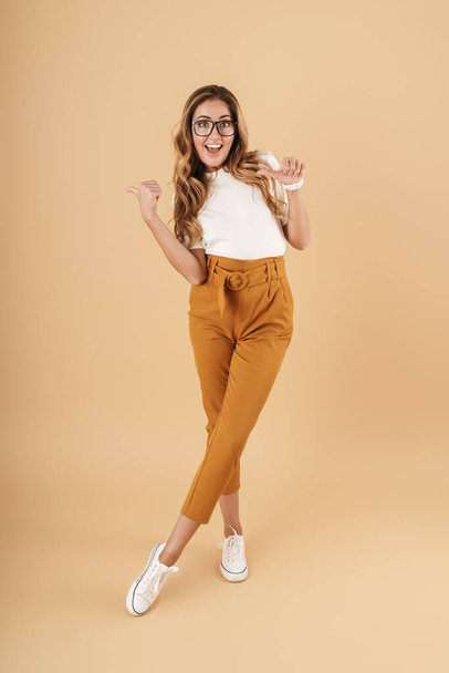 Full length image of stylish woman smiling and pointing fingers at copyspace - Fotó, kép