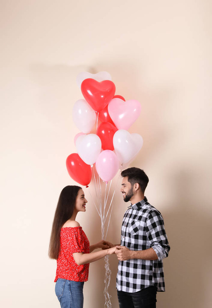Beautiful couple with heart shaped balloons on beige background. Valentine's day celebration - Zdjęcie, obraz