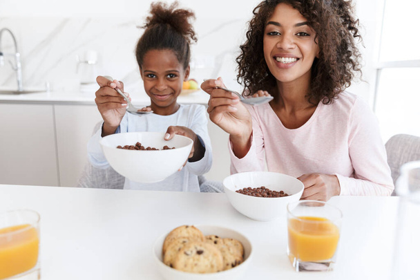 Image of american woman and her daughter having breakfast in kit - Fotó, kép