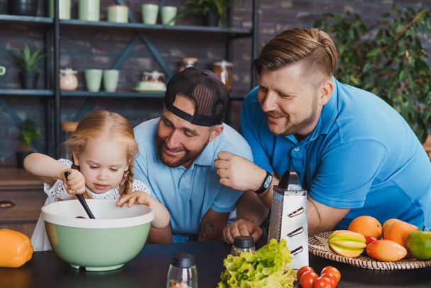 Gay parents looking how their little daughter cooking - Photo, image