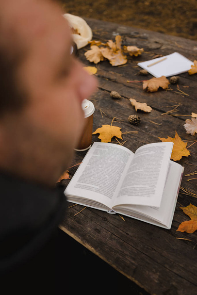 Чоловіча жінка читає книгу в осінньому парку, п'є каву. Крупним планом над плечем, розмитим. вид зверху, зберегти простір. Побачили руки. У темному ретро стилі
 - Фото, зображення