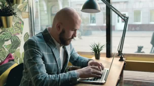 bald man in a jacket works on a computer - Filmati, video