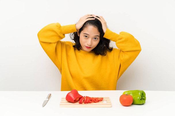 Joven chica asiática con verduras en una mesa con expresión facial sorpresa
 - Foto, Imagen