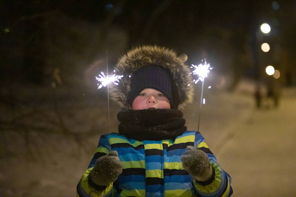 mały chłopiec w zimowym parku miejskim w ciepłym płaszczu z ogniem - Zdjęcie, obraz